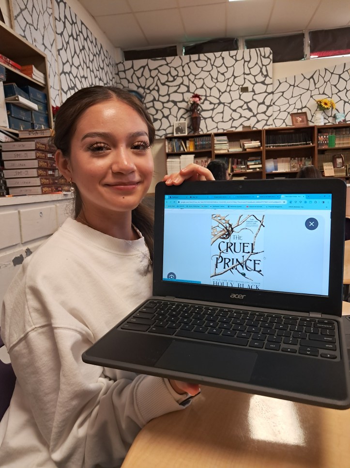 Anayeli Salazar holding a computer with the cover of the book The Cruel Prince by Holly Black